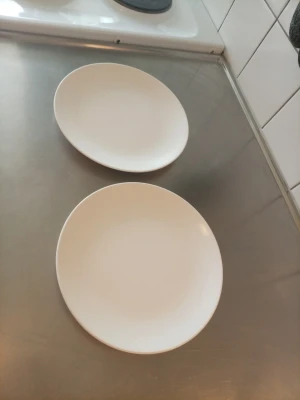 Två vita runda tallrikar - Säljer två stilrena vita tallrikar med rund form. Perfekta för både frukost och middag. Tallrikarna är gjorda i keramik och har en enkel, modern design som passar in i de flesta kök.