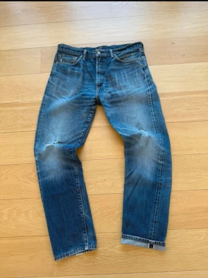 Levi 508 med slitningar  - Säljer ett par blå jeans med raka ben och snygga slitningar vid knäna och låren. Jeansen har klassisk femficksdesign och är gjorda i denim med en tvättad look. Perfekta för en avslappnad och trendig stil.