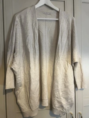 Ljusbeige oversized kofta - En ljusbeige, oversized kofta med öppen front och långa ärmar. Koftan har en avslappnad passform och ribbade muddar vid ärmslut och nederkant. Perfekt att slänga på sig över en t-shirt eller topp för en chill look.