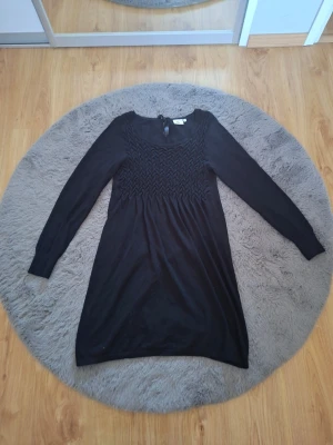 Svart långärmad klänning Isolde - Svart klänning från Isolde med lång ärm och smockad överdel. Klänningen har rund halsringning och en enkel, rak passform som ger en stilren look.