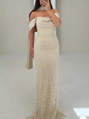 Champagnefärgad långklänning med paljetter - Elegant långklänning i champagnefärg med glittriga paljettdetaljer. Klänningen har offshoulder-design med draperad överdel och lång släp. Endast använd 1 gång. Storleken är 38 men passar mig som brukar ha 34-36🩷 