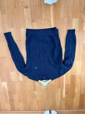 Mörkblå kabelstickad tröja - Snygg mörkblå kabelstickad tröja med rund hals och långa ärmar. Tröjan har ribbade muddar vid hals, ärmslut och nederkant. Perfekt för dig som gillar klassisk och stilren design.