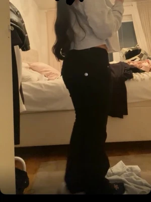 Svarta jeans med lågmidja och silver knappar bakom - Säljer ett par svarta jeans med låg midja och utsvängda ben. Jeansen har vart använda några gånger, säljer eftersom jag vuxit ur. Passar perfekt och är väldigt sköna. Materialet är bomullsdenim och rekommenderas att tvättas på 30 grader.