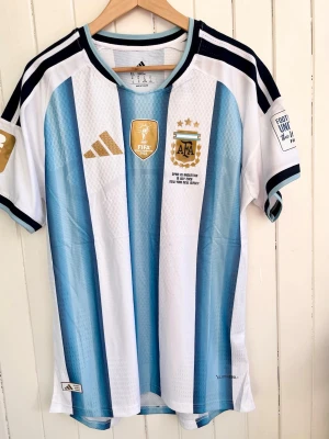 Argentina - VM-final 2026 - Player version - Säljer en (snart) klassisk fotbollströja, Argentinas VM-finaltröja från 2026. Tröjan är en reprint i nyskick med emblem och patchar av högsta kvalité.   Storlek:XL, men liknar mer L/XL. Denna tröja är en player version, tröjan som spelarna själva använder. Bättre kvalité och passform (slim fit).  Kan skickas snabbt eller hämtas i Majorna i Göteborg.    #fifa #WorldCup #panini #fotboll #fifa #Argentina #panini #fotboll #fashion #Messi #Barcelona #Ronaldo