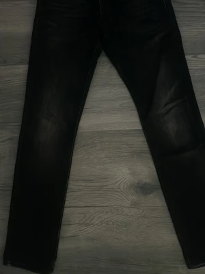 Svarta slim fit jeans - Säljer ett par svarta slim fit jeans med diskreta slitningar framtill. Jeansen har klassisk femficksdesign och raka ben. Materialet är denim med lite stretch för skön passform. Perfekta till en avslappnad streetwear-look. 32 midjan och 32 längd 