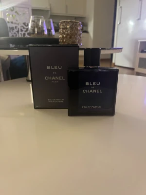 Bleu de Chanel Eau de Parfum (kom med bud) - Bleu de Chanel Eau de Parfum är en elegant herrparfym i en stilren, mörkblå glasflaska med matchande förpackning. Doften är maskulin och modern, perfekt för dig som gillar exklusiva och tidlösa parfymer. Flaskan har en fyrkantig form och silverfärgad text. Kom gärna med bud. Locket är lite trögt men funkar som det ska
