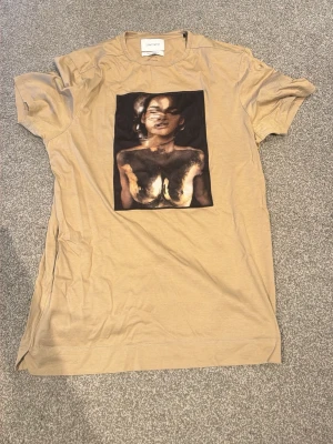 Beige t-shirt från Limitato - Beige t-shirt från Limitato med ett stort konstnärligt tryck framtill. T-shirten har rund halsringning och är tillverkad i mjuk bomull. Perfekt för dig som vill sticka ut med en unik och stilren look.