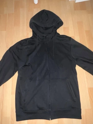 Svart zip hoodie från Clique - Säljer en svart hoodie från Clique i storlek M. Hoodien har dragkedja framtill, två fickor och justerbar huva med snören. Tillverkad i mjukt material som känns skönt mot huden. Perfekt för en avslappnad och stilren look.