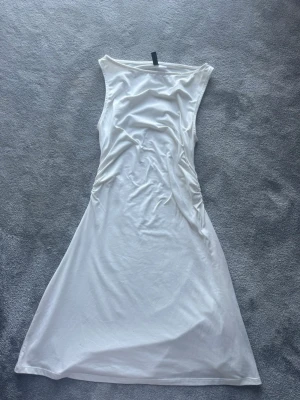 Vit långklänning med rynkade sidor - Säljer en elegant vit långklänning med ärmlös design och rynkade detaljer längs sidorna. Klänningen har en mjuk och följsam passform som ger en snygg siluett. Perfekt för dig som gillar stilrena och enkla plagg.