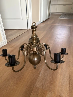 Antik mässingsljuskrona med detaljer - Säljer en antik ljuskrona i mässing med plats för fem ljus. Ljuskronan har vackra ornament och detaljerade ansikten i metall runt centrumdelen. Klassisk rund form och böjda armar ger en elegant känsla. Perfekt som inredningsdetalj för dig som gillar vintage och unika föremål. Kolla gärna mina andra annonser❗️