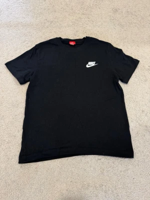 Svart Nike t-shirt  - Säljer en svart t-shirt från Nike med klassisk vit logga på bröstet. T-shirten har rund hals och korta ärmar, perfekt för en clean och sportig look. Tillverkad i mjuk bomull som känns skön mot huden.