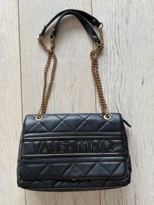 Svart handväska Valentino - Snygg svart quiltad handväska från Valentino med guldfärgade kedjor och axelband i läder.