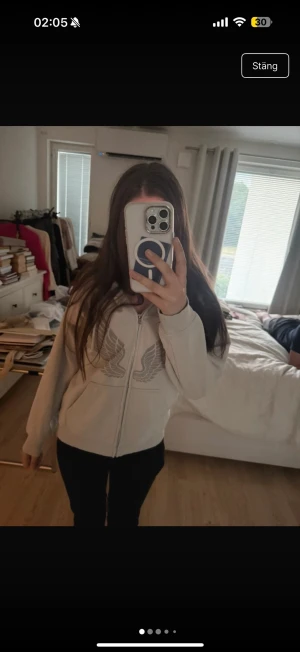 Grå hoodie med vingar och dragkedja - Säljer en grå hoodie med dragkedja och stora tryckta vingar på framsidan. Hoodien har huva med dragsko och en stor magficka. Perfekt för en chill och avslappnad stil. Materialet ser ut att vara mjukt och bekvämt, troligen bomullsblandning.