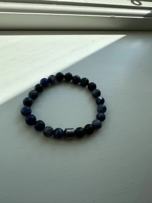 Blått pärlarmband med metallpärla - Snyggt armband med runda blå pärlor i olika nyanser och en större metallfärgad pärla som detalj. Elastiskt band gör det enkelt att ta på och av. Perfekt accessoar för att lyfta din stil.