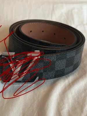 Svart och grått rutigt bälte - Snyggt bälte i svart och grått med rutigt mönster och silverfärgat spänne. Bältet har en bred design och är gjort i skinn. Perfekt för att lyfta vilken outfit som helst. VIKTIGT: ett hål är lite skadat, PRISET KAN DISKUTERAS.