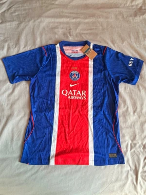 PSG matchtröja O. Dembélé #10 - Snygg PSG matchtröja i blått och rött med vita detaljer. Framsidan har Qatar Airways-logga och PSG-emblem, baksidan har O. Dembélé och nummer 10. Tillverkad i lätt och ventilerande material, perfekt för fotboll eller träning.