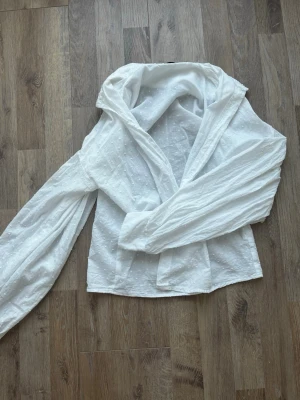 Vit blus med struktur från SHEIN - Säljer en vit blus från SHEIN i storlek XS. Blusen har långärmad design, lätt puffade ärmar och ett tunt, prickigt strukturmönster i tyget. Materialet är tunt och luftigt, perfekt för en trendig och avslappnad look💓