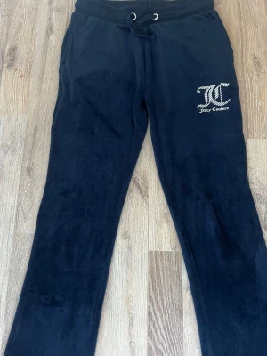 Svarta velourbyxor Juicy Couture - Mysiga svarta mjukisbyxor från Juicy Couture i mjuk velour. Byxorna har dragsko i midjan och ett glittrigt Juicy Couture-logotryck på ena benet. Perfekta för chill dagar eller när du vill ha en avslappnad look💗