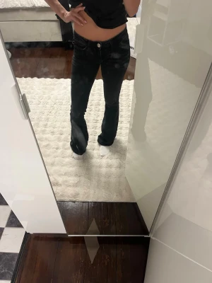 Svarta bootcut jeans med låg midja - Säljer ett par svarta bootcut jeans med låg midja och klassiska fem fickor. Jeansen har en snygg passform som sitter tajt över låren och släpper ut vid vaden. Perfekta för dig som gillar en trendig och avslappnad stil.
