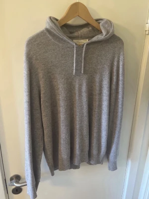 Ljusgrå hoodie i mjukt material - Säljer en stilren ljusgrå hoodie med huva och dragsnören. Hoodien har en avslappnad passform och är tillverkad i ett mjukt, stickat material som känns riktigt skönt mot huden. Perfekt för dig som gillar en enkel men snygg look.