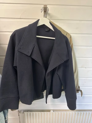 Mörkblå kappa från Gina Tricot - Stilren mörkblå kappa från Gina Tricot i storlek S. Kappan har bred krage, rak passform och är tillverkad i ett mjukt, tjockare tyg som passar perfekt till kyligare dagar. 