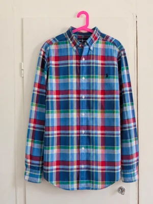 Polo Ralph Lauren rutig skjorta - Färgglad långärmad skjorta från Polo Ralph Lauren med rutigt mönster i blått, rött, grönt och vitt. Mörkblå broderad Polo-logga på bröstet samt klassisk button-down-krage. Snygg modell som passar super bra  till jeans eller chinos. 📏 Storlek: L (14-16) ✨ Skick: Mycket bra utan defekter! Hör av dig vid frågor eller om du vill ha mått/fler bilder! 📦