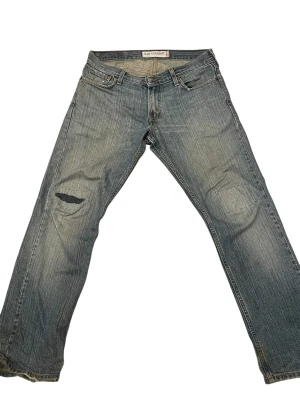 Levi's Slim Straight 511 jeans  - Snygga blå Levi's 511 Slim Straight jeans med slitningar och ett hål på vänster lår. Klassisk femficksmodell med dragkedja och knappgylf. Jeansen har en rak passform och är tillverkade i denim med en cool tvätt.