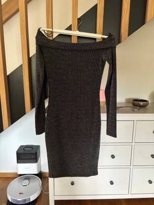 Svart glittrig offshoulder klänning - Snygg svart glittrig tunn klänning från Vera & Lucy med offshoulder-modell och lång ärm. Klänningen är figurnära och kort, perfekt för dig som vill sticka ut med lite extra glitter. Materialet känns stretchigt och bekvämt. Passar xs
