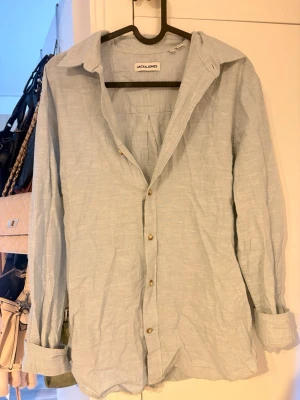 Ljusblå linneskjorta från Jack & Jones - Snygg ljusblå skjorta i linne från Jack & Jones. Skjortan har klassisk krage, långa ärmar och knappar framtill. Perfekt för en avslappnad men stilren look.