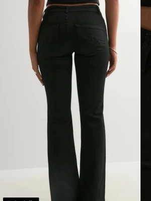 Svarta bootcut jeans med hög midja - Snygga svarta bootcut jeans med hög midja och klassiska fem fickor. Jeansen har en figurnära passform upptill och utsvängda ben. Materialet ser ut att vara stretchigt denim för extra komfort. Perfekta för en trendig och avslappnad look. Helt nya med prislapp 