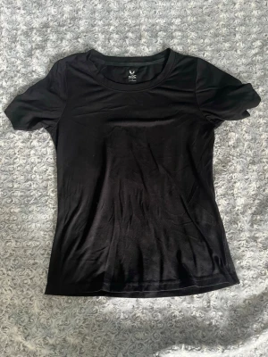Svart tränings-tshirt dam - En svart, figurnära tränings-tshirt med rund hals och korta ärmar. Tillverkad i ett mjukt och stretchigt funktionsmaterial som andas, perfekt för gymmet eller löprundan.