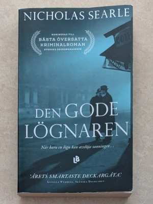 Den gode lögnaren av Nicholas Searle - Spännande kriminalroman av Nicholas Searle med mörkblått omslag och mystisk stämning. Boken handlar om svindlaren Roy Courtnay och hans livs största kupp. Perfekt för dig som gillar psykologiska thrillers och deckare.