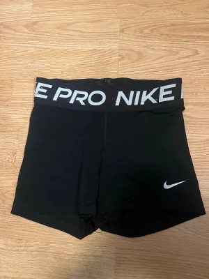 Svarta Nike Pro shorts - Säljer ett par svarta Nike Pro shorts med vit logga och bred elastisk midja där det står 'NIKE PRO'. Perfekta för träning och sport, tillverkade i stretchigt material som ger bra passform och rörelsefrihet. Dom är väl använda men inget slitage som försör plagget