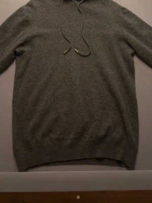 Mörkgrå hoodie i mjukt material - En stilren mörkgrå hoodie med huva och dragsnören. Hoodien har långa ärmar och ribbade muddar vid ärmslut och nederkant. Materialet ser ut att vara mjukt och skönt, perfekt för en avslappnad look.