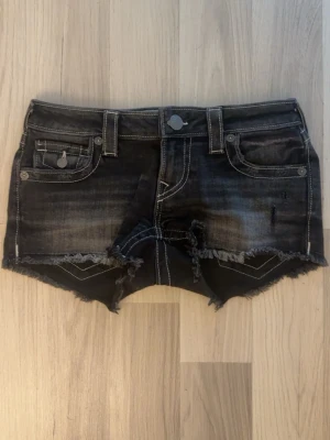 Svarta jeansshorts True Religion - Snygga svarta jeansshorts från True Religion med slitna detaljer. Shortsen har fem fickor, dekorativa sömmar och knappar med logga. Perfekta för en avslappnad och trendig stil. Använt en gång