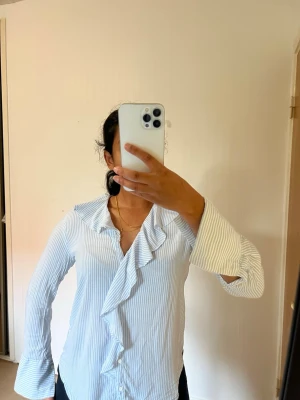 Zara Blåvit randig blus - Superfin ljusblå/vit randig skjorta från Zara Basic Collection 💙🤍 Priset kan sänkas vid snabb affär.  ✨ Snygg volangdetalj framtill och vid kragen ✨ Långa ärmar ✨ Ljusblå & vit smalrandig ✨ Feminin men samtidigt stilren modell Perfekt till jeans, kostymbyxor eller kjol – funkar både till vardags, kontoret och en mer uppklädd look.  