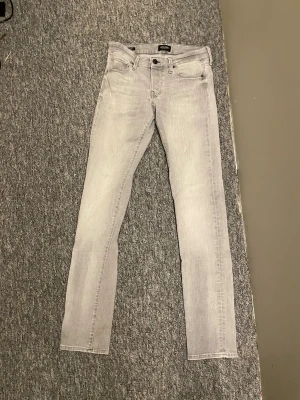 Ljusgrå slim fit jeans - Snygga ljusgrå jeans i slim fit-modell med klassisk femficksdesign och dragkedjegylf. Jeansen har en modern tvätt och raka ben som smalnar av. Perfekta för dig som vill ha en stilren och enkel look till vardags. Storlek 29/34