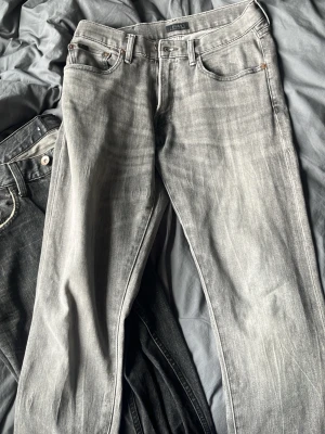 Grå tvättade raka jeans - Säljer ett par grå jeans med tvättad look och raka ben. Klassisk femficksmodell med bälteshällor och knappgylf. Jeansen har snygga slitningar och kontrastsömmar, perfekta för en avslappnad stil.