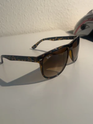 RayBan boyfriend leopardmönster - Snygga Ray-Ban solglasögon med leopardmönstrad båge i bruna och gula toner. Modellen har stora, fyrkantiga glas och klassisk logga på sidan. Perfekta för att lyfta din stil med en cool och trendig vibe.