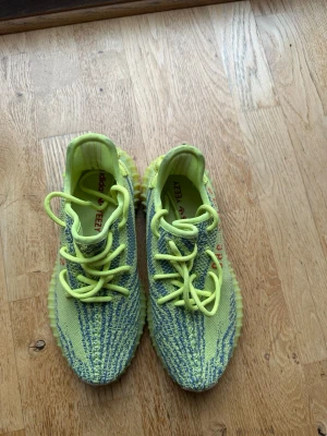 Adidas Yeezy Boost 350 V2 gul/blå - Säljer ett par Adidas Yeezy Boost 350 V2 i färgen gul och blå med inslag av grått. Skorna har en stickad ovandel, klassiska Yeezy-detaljer och gula snören. Sulan är i matchande gul ton och ger en sportig vibe. Perfekta för dig som vill sticka ut. Jätte bra skick 
