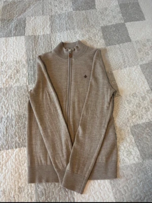 Morris fullzip tröja  - Snygg beige ziptröja med ståkrage och diskret broderad detalj på bröstet. Tröjan har hel dragkedja framtill och ribbade muddar vid ärmslut och nederkant. Perfekt för lager på lager och enkel att matcha med olika outfits.priset kan diskuteras och skriv vid några frågor 