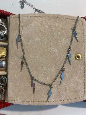 Halsband med blixtberlocker i silverfärg - Snyggt halsband i silverfärgad metall med flera små blixtformade berlocker längs kedjan. Kedjan är tunn och har justerbar längd. Perfekt för dig som gillar edgy och trendiga accessoarer med en unik touch.
