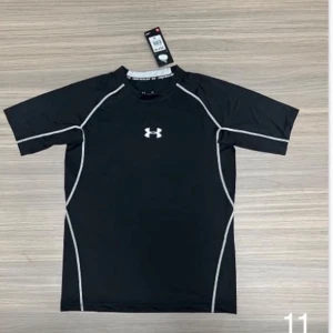 Svart träningströja från Under Armour - Snygg svart träningströja från Under Armour med vita kontrastsömmar och logga på bröstet. Tillverkad i ett stretchigt funktionsmaterial som andas, perfekt för gymmet eller löprundan. Kortärmad modell med sportig design.