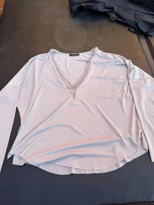 Ljusblå ribbad topp från Zara - Snygg ljusblå långärmad topp från Zara med ribbad struktur och v-ringad hals. Perfekt till jeans eller kjol för en chill och trendig look. Materialet känns mjukt och följsamt mot huden.