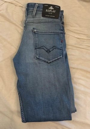 Ljusblå jeans från Replay 30/32 - Snygga ljusblå jeans från Replay med klassisk femficksdesign och diskreta slitningar. Jeansen har raka ben och tydliga sömmar på bakfickorna. Perfekta för en avslappnad och trendig stil. Modellen är Anbass 