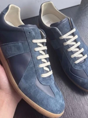 Blå Maison Margiela sneakers - Snygga sneakers från Maison Margiela i blå mocka och läder med vita snören och klassisk gummisula. Skorna har en låg silhuett och retroinspirerad design som passar perfekt till streetwear och casual outfits. Skorna är använda 1 gång, verkligen toppskick. Storlek 44. Kommer utan box då jag köpt dessa på andra hand.