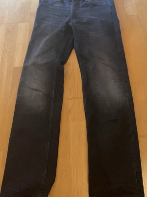 Svarta raka jeans med tvättade detaljer - Säljer ett par svarta jeans med raka ben och snygga tvättade detaljer på framsidan. Jeansen har klassisk femficksmodell och normal midja. Materialet är denim med lite stretch för skön passform. Perfekta till en avslappnad streetstil.