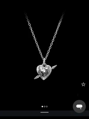Silverhalsband med hjärthänge och pil - Snyggt halsband i silverfärg med ett hjärthänge som har en pil genom sig. Hänget har en lite rå, ojämn yta som ger en cool och unik look. Kedjan är tunn och stilren, perfekt för att lyfta vilken outfit som helst.