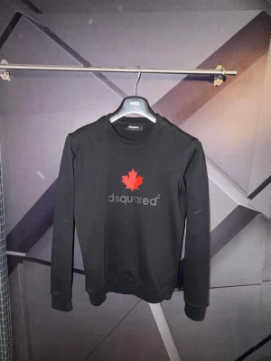 Dsquared tröja - Svart långärmad topp från Dsquared2 med röd lönnlöv-tryck och logga på bröstet. Klassisk rund halsringning och ribbade muddar vid ärmslut och nederkant. Perfekt för dig som gillar stilrena och trendiga plagg.
