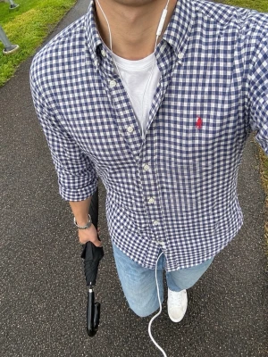 Blårutig skjorta från Ralph Lauren - Säljer en klassisk blårutig skjorta från Ralph Lauren i modellen Custom Fit. Skjortan har långa ärmar, knappar framtill och den ikoniska röda loggan broderad på bröstet. Perfekt till jeans eller chinos för en clean och stilren look.
